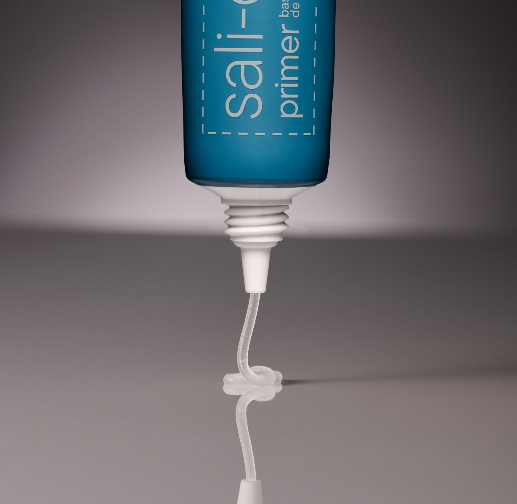 A close up photo of a teal-colored tube of makeup primer with the primer being squeezed onto a reflective surface