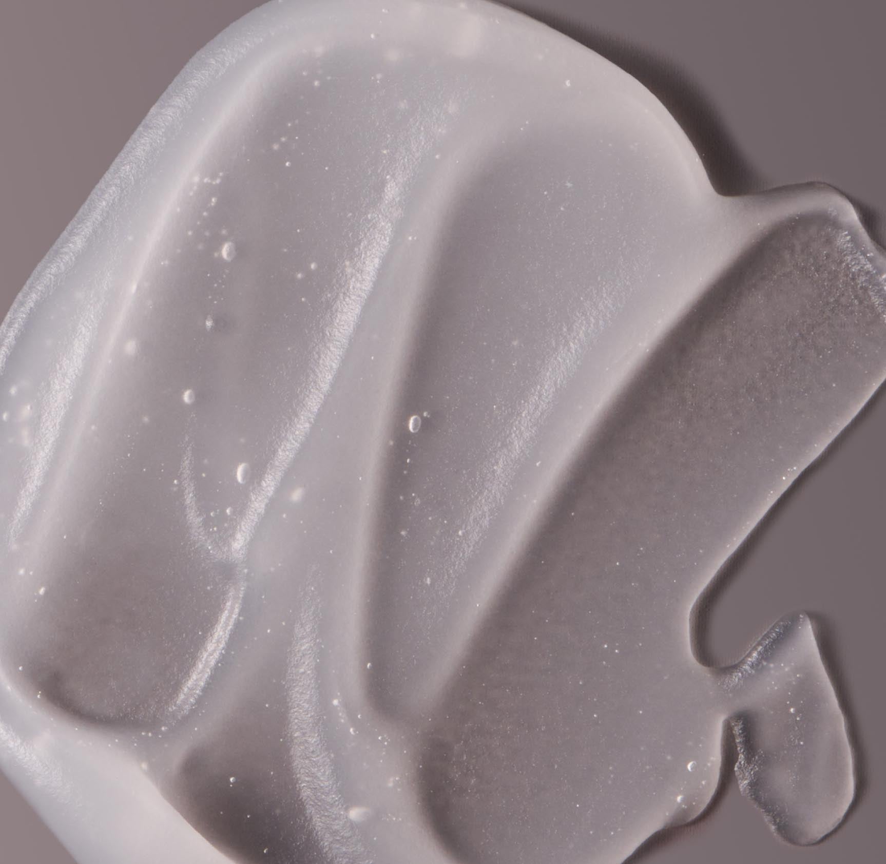 Close up photo of a blob of semi-transparent white makeup primer on a gray surface