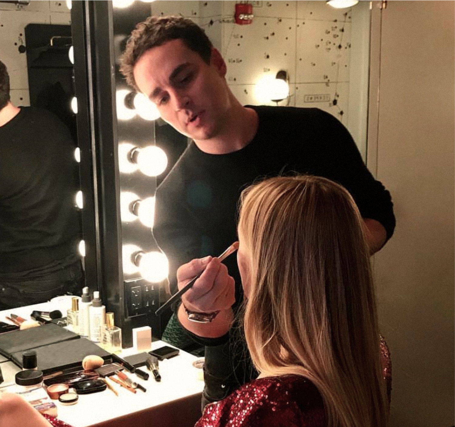 makeup artist applying makeup on model wearing a red dress while seated.