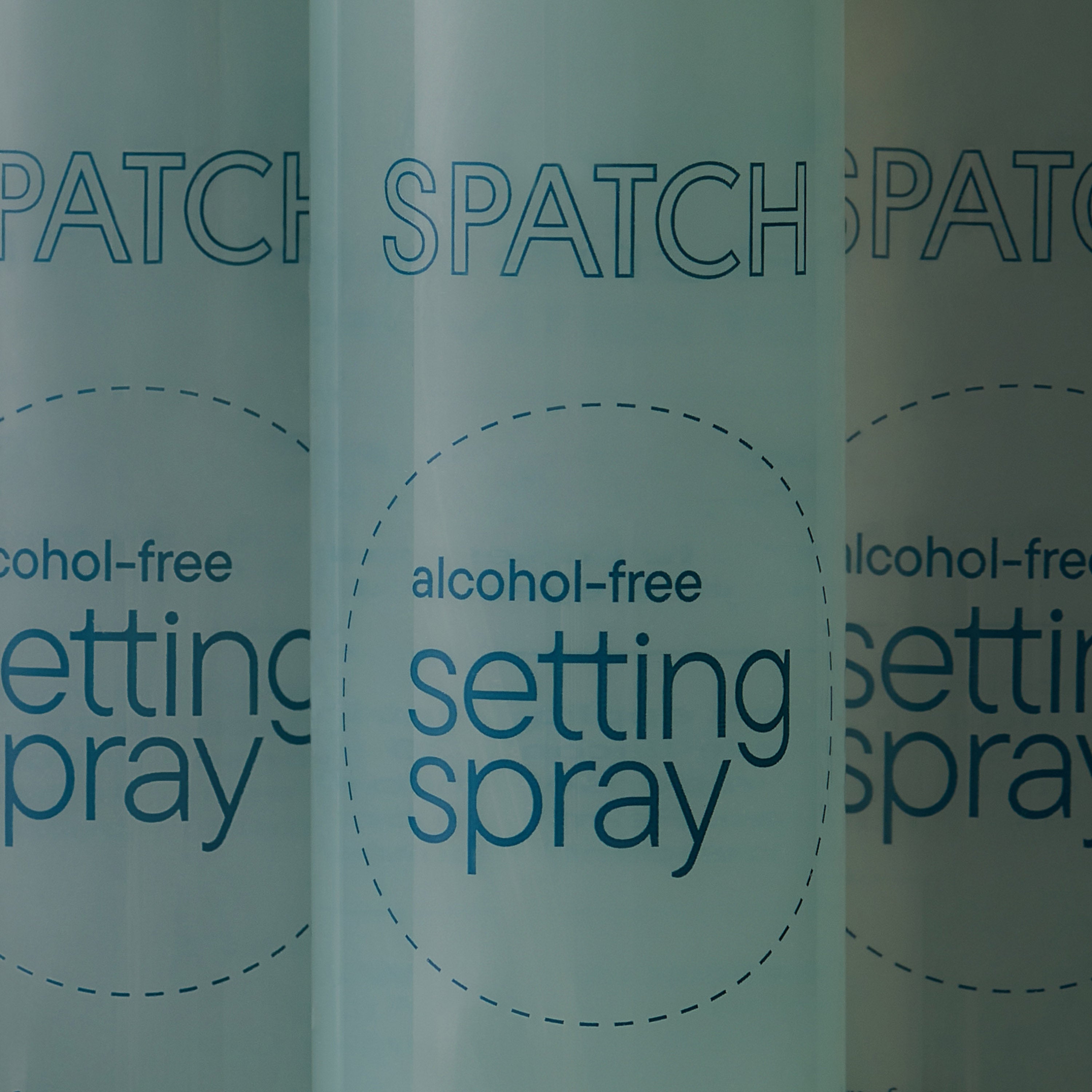 Closeup photo of three bottles of aqua-colored makeup setting spray with the words &quot;SPATCH alcohol-free setting spray&quot; on the bottles