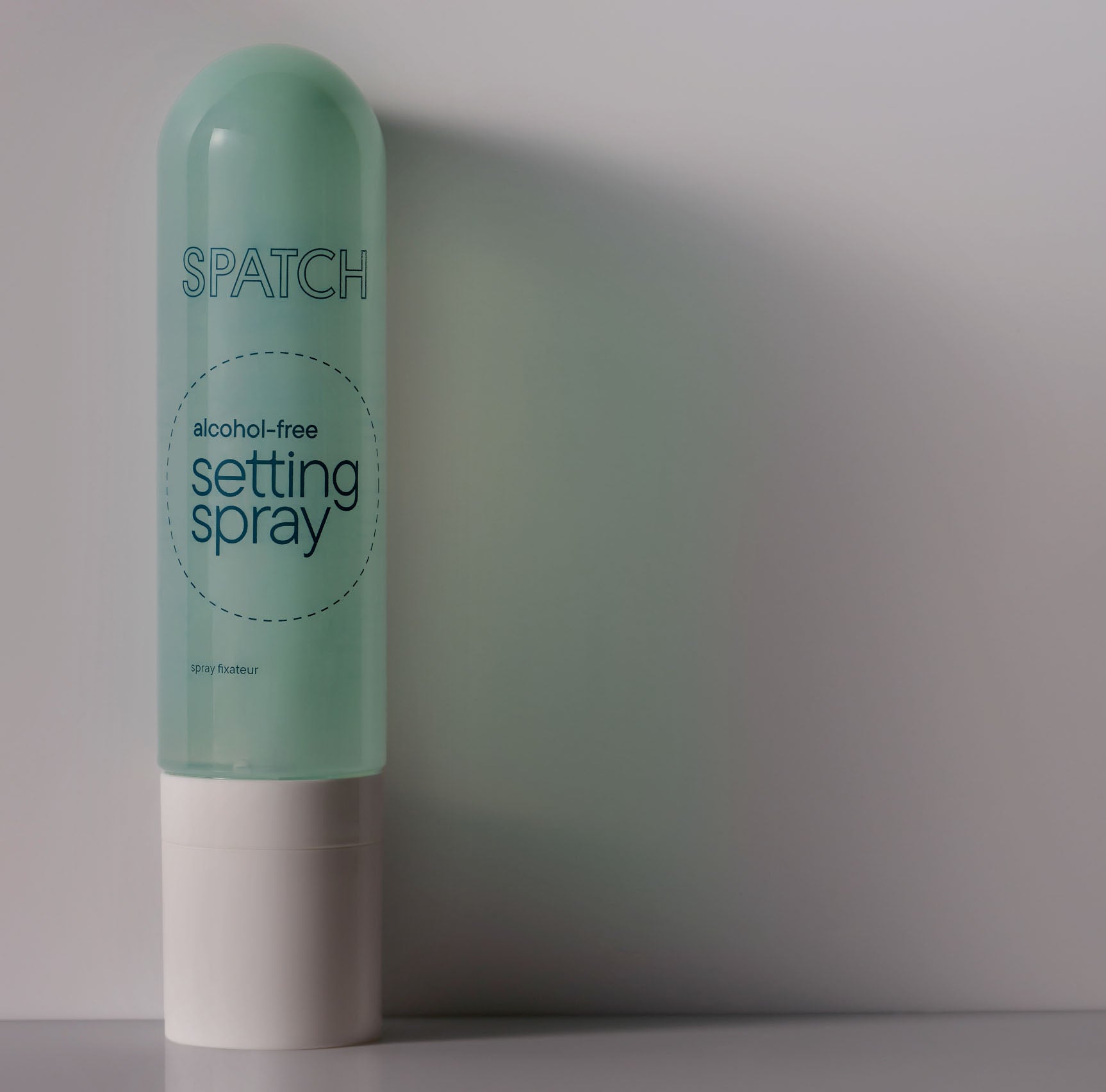 A transparent aqua green bottle with a logo reading SPATCH and the product name &quot;alcohol-free setting spray&quot; in a circle on a light gray background